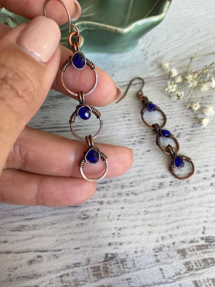 a person is holding onto some kind of blue and silver earrings on a white table