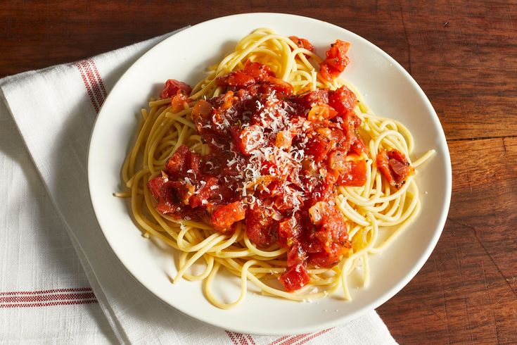 a plate of spaghetti with sauce and parmesan cheese on the side, sitting on a wooden table