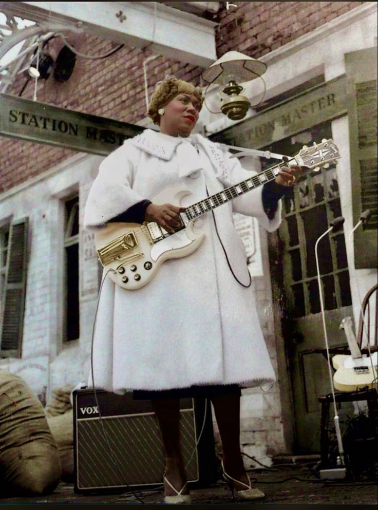 a woman standing in front of a building holding a guitar