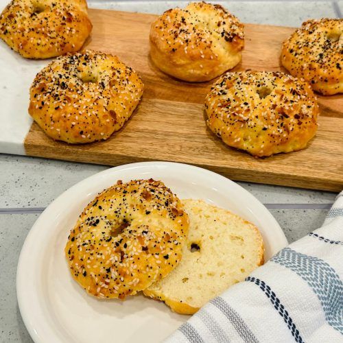 several bagels on a plate next to a towel and some other breads in the background