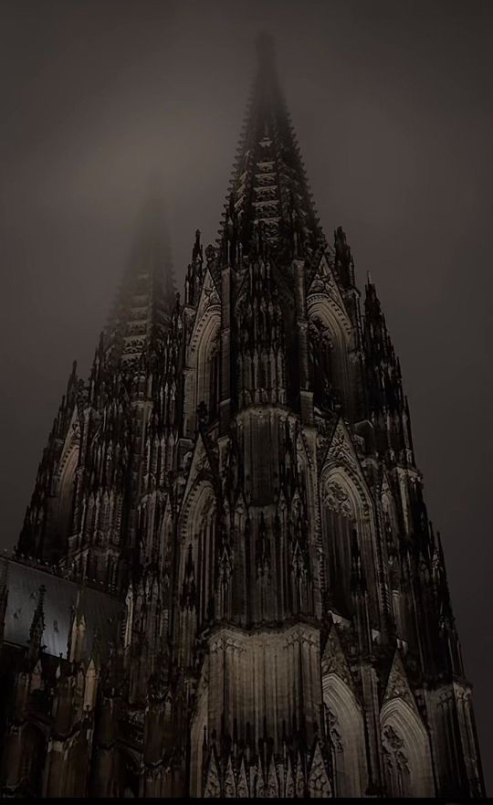 an image of a gothic cathedral in the foggy night with light coming from it