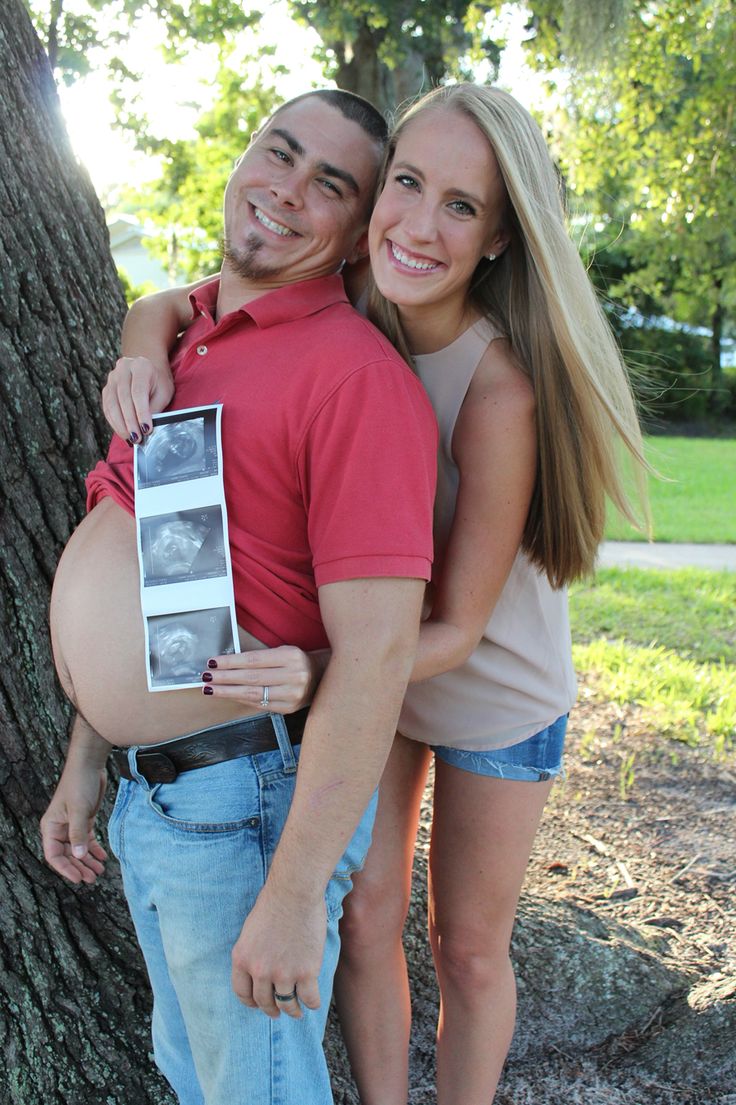 a man and woman hugging each other in front of a tree with their pregnant belly exposed