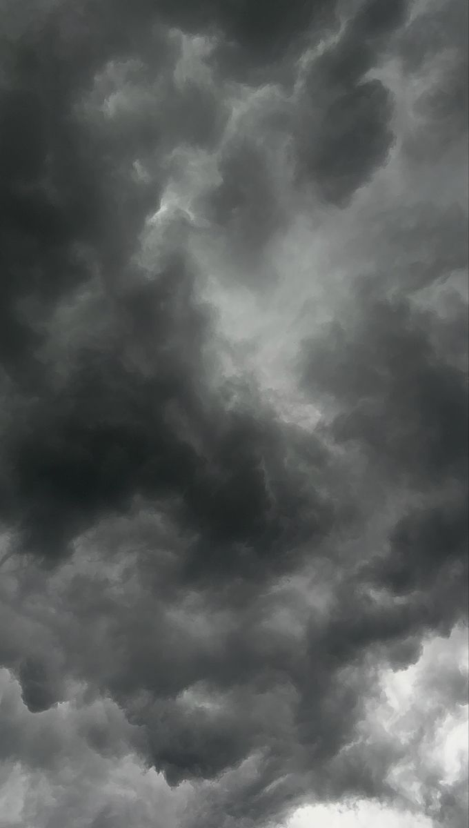 black and white photograph of storm clouds in the sky with an airplane flying above it