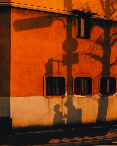 the shadow of two people standing in front of an orange building on a city street