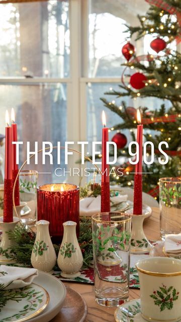 a christmas table setting with candles, dishes and cups in front of a decorated christmas tree