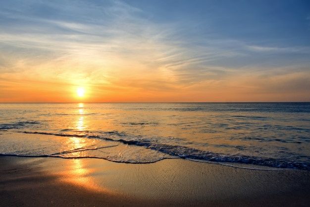 the sun is setting over the ocean with waves coming in to shore and blue sky