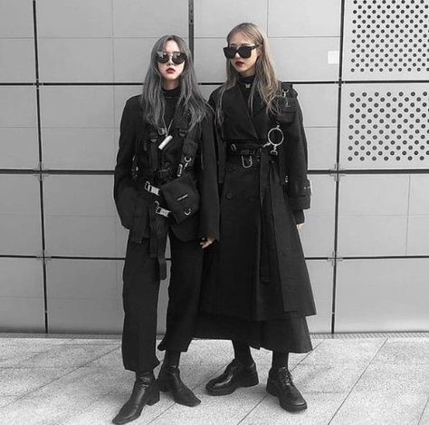 two women standing next to each other in front of a wall wearing black clothing and sunglasses