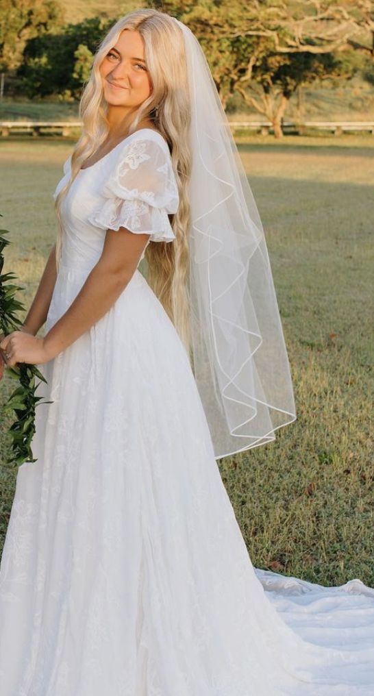 a woman in a white wedding dress and veil posing for the camera with her hand on her hip