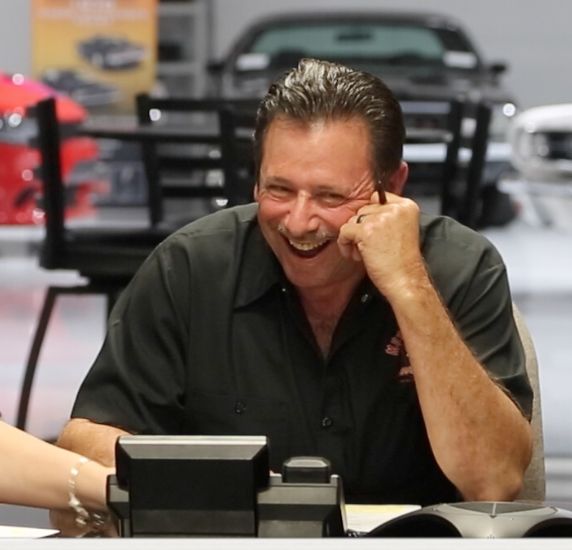 a man laughing while sitting at a table in front of a laptop computer with his hand on his face