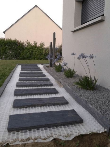 an outdoor walkway made out of concrete and gravel with flowers growing on the side of it