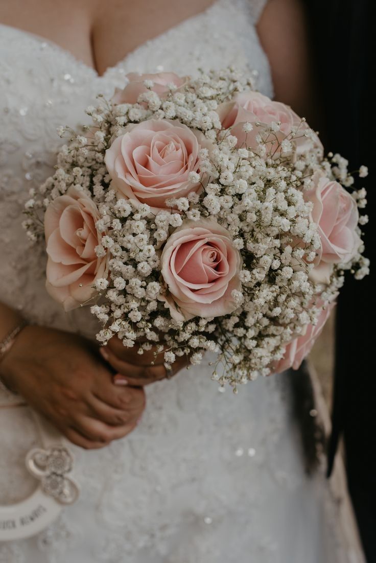 a bride holding a bouquet of pink roses and baby's breath