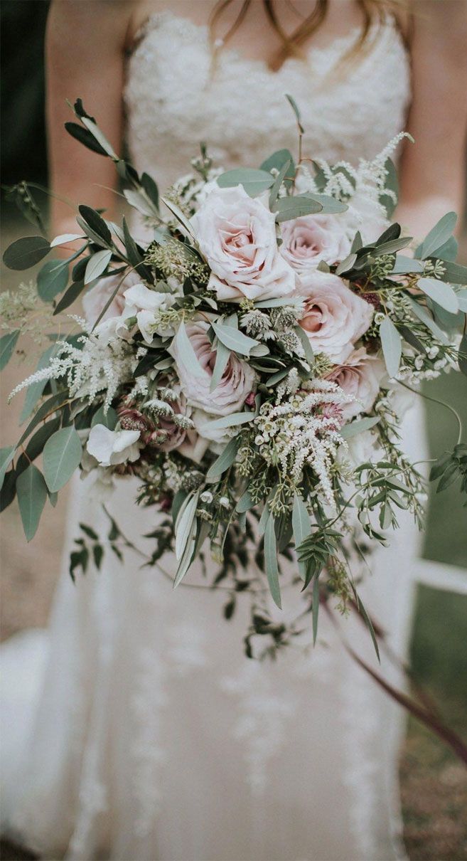 a bride holding a bouquet of flowers and greenery