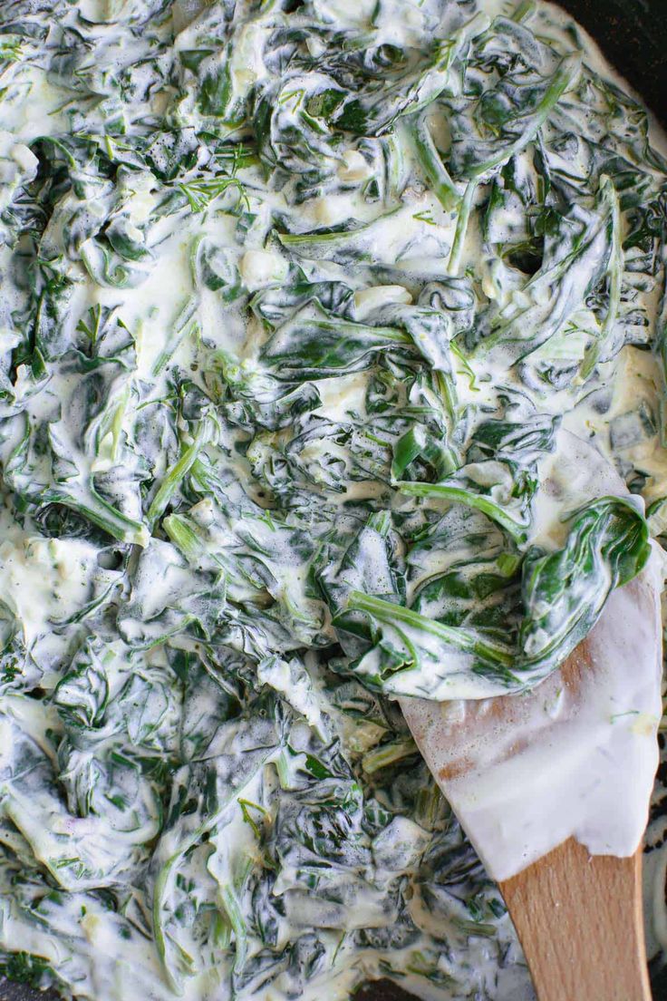 spinach and cheese dip in a skillet with a wooden spoon on the side