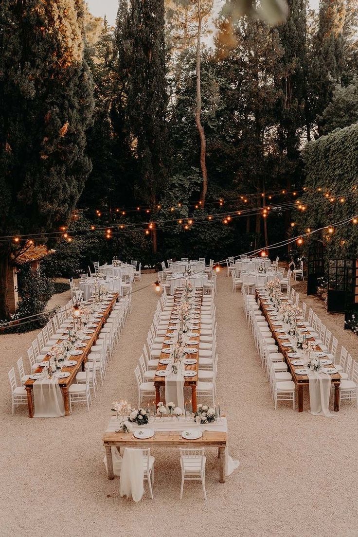 an outdoor wedding reception setup with long tables and white linens, lights strung from the trees