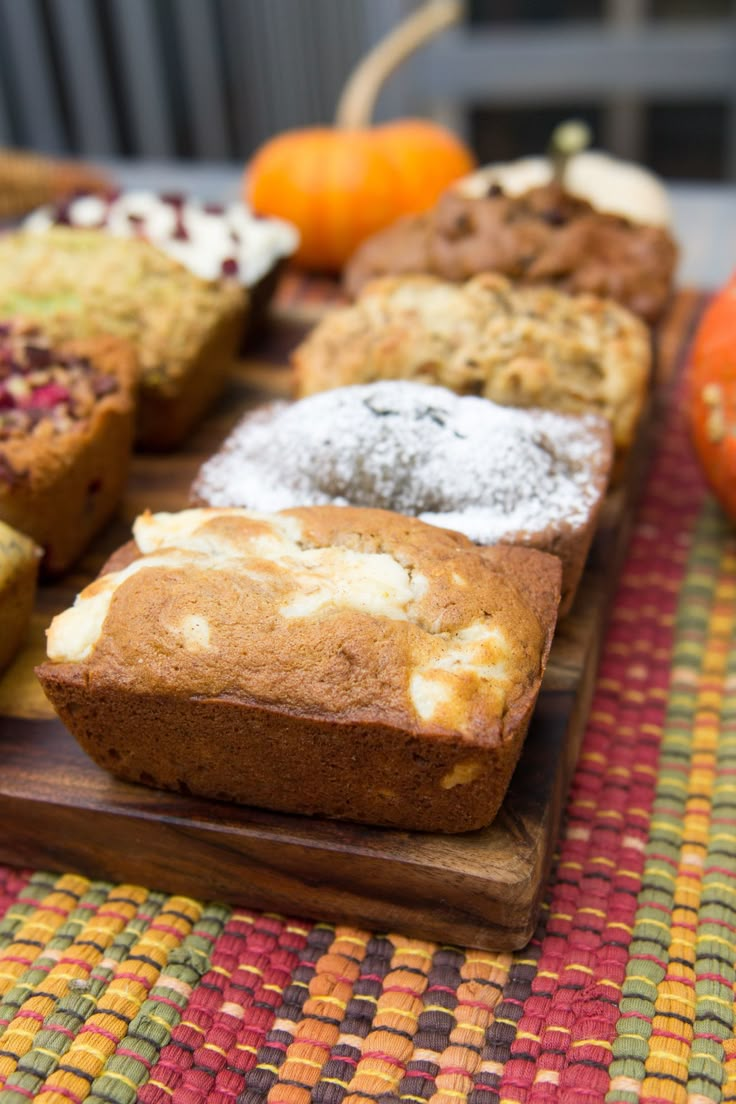 there are many different types of bread on this wooden platter with oranges in the background