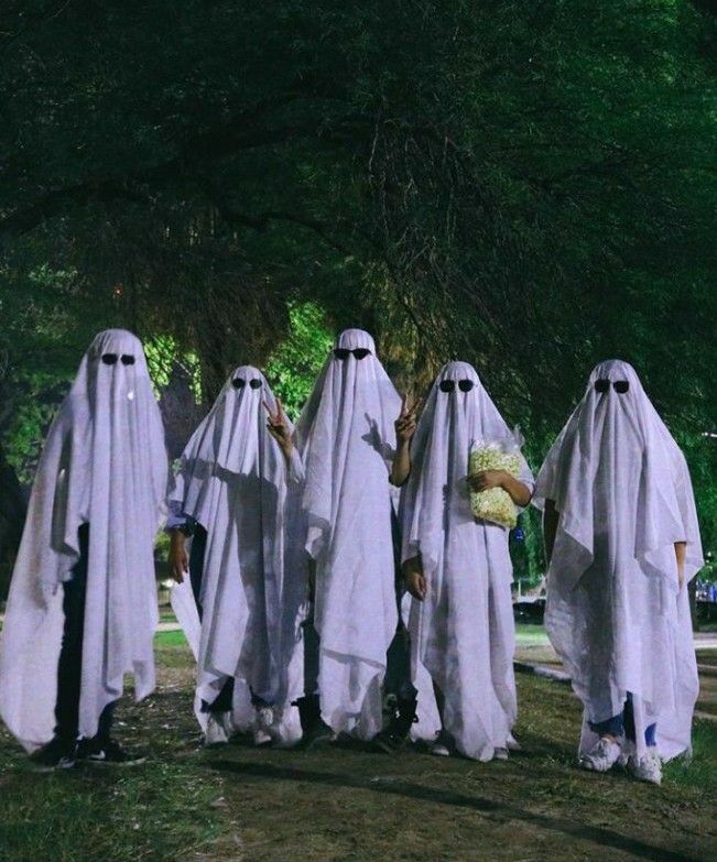 four people in white robes walking down a street together with flowers on their heads and hands