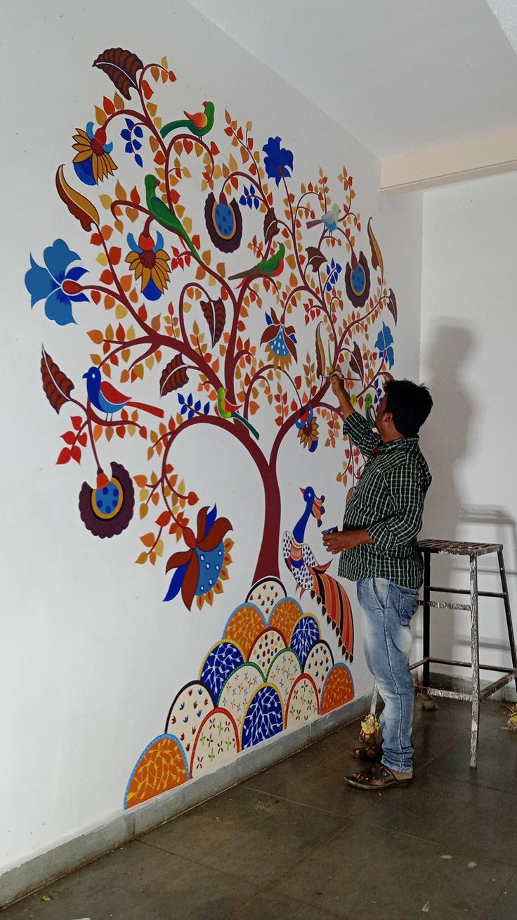 a man is painting a tree on the wall with colorful designs and birds around it