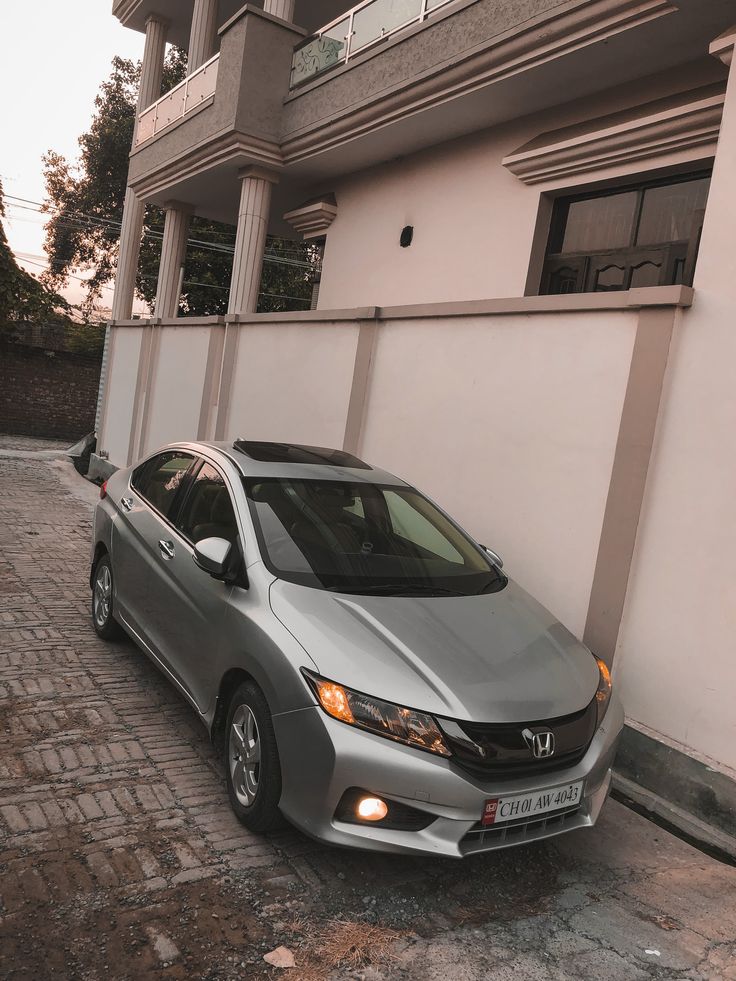 a silver car parked in front of a white wall next to a tall building with windows