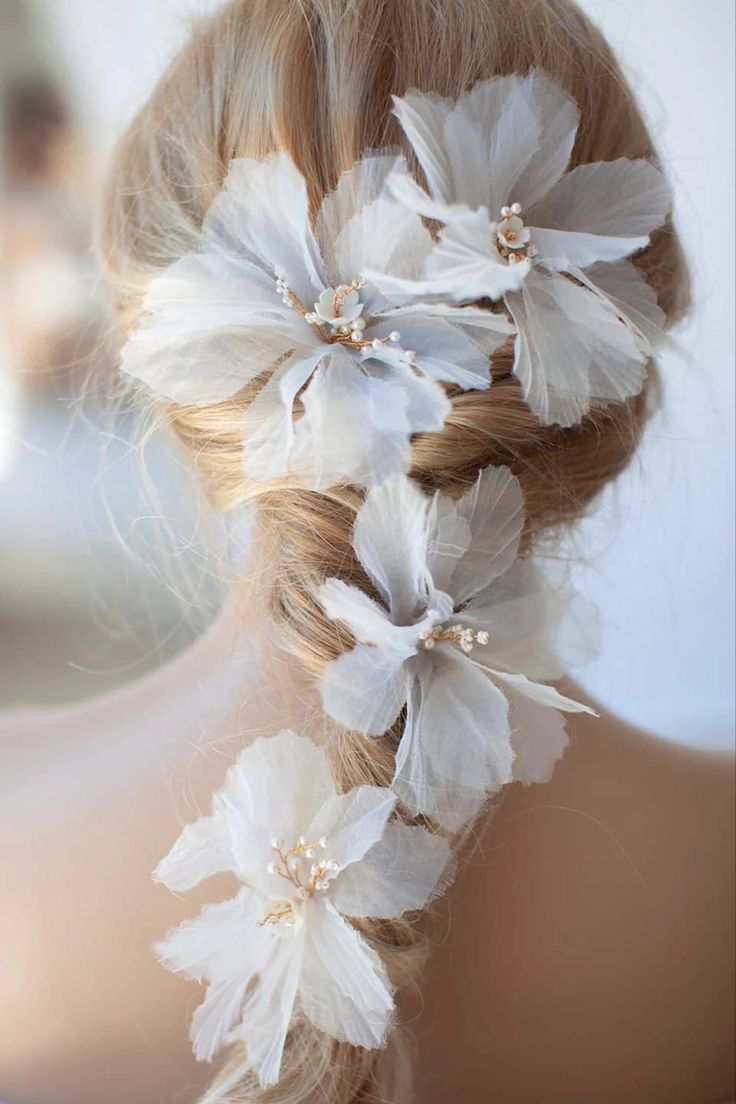 a woman's hair with white flowers and pearls in her hair is seen from the back