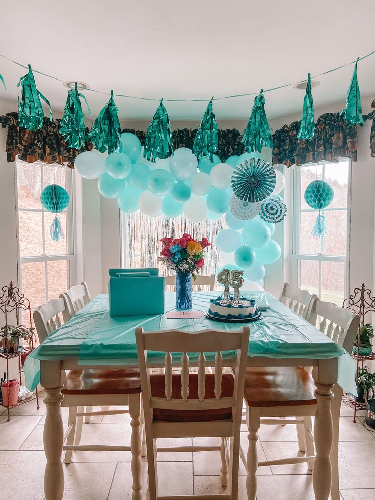 a dining room table with blue and white balloons hanging from it's ceiling over it