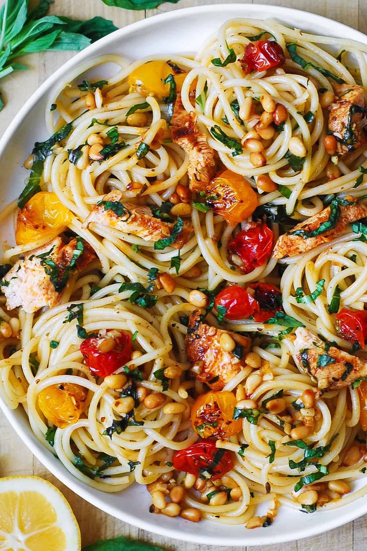 a white bowl filled with pasta and chicken on top of a table next to sliced lemons