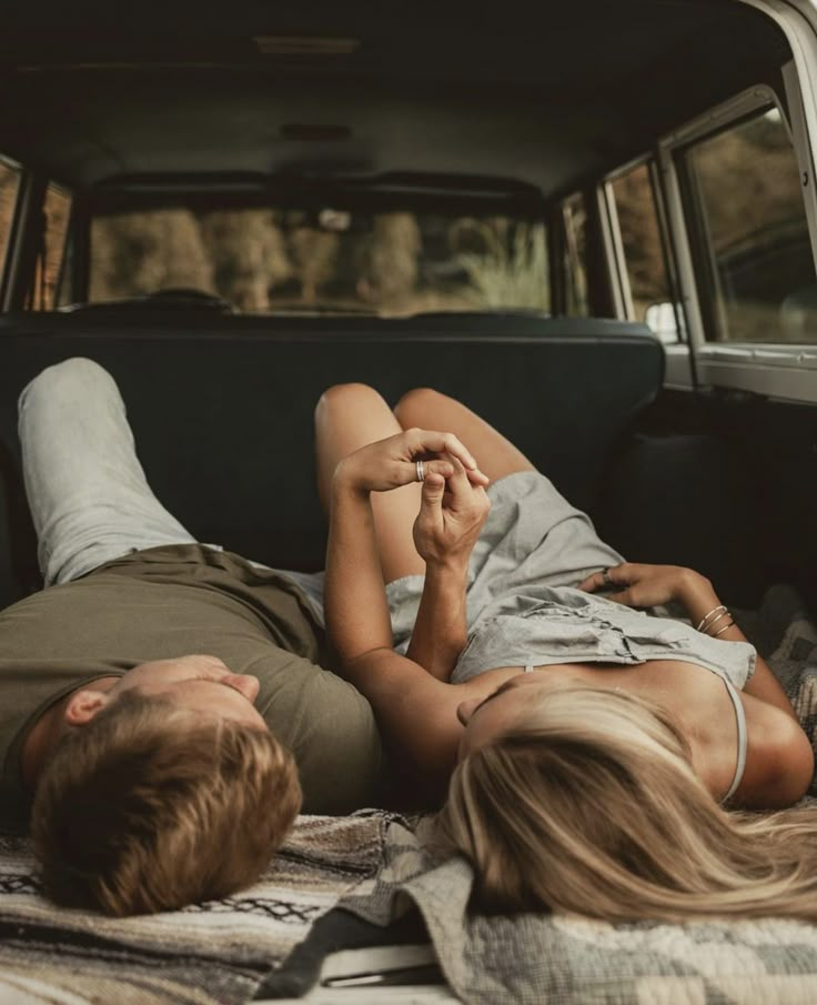 a man and woman laying in the back of a pick up truck with their hands together