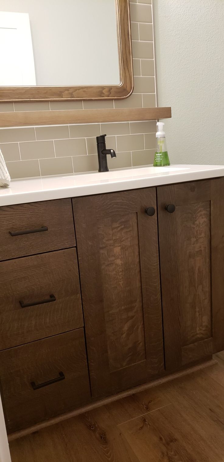 a bathroom vanity with wooden cabinets and white counter tops, in front of a large mirror