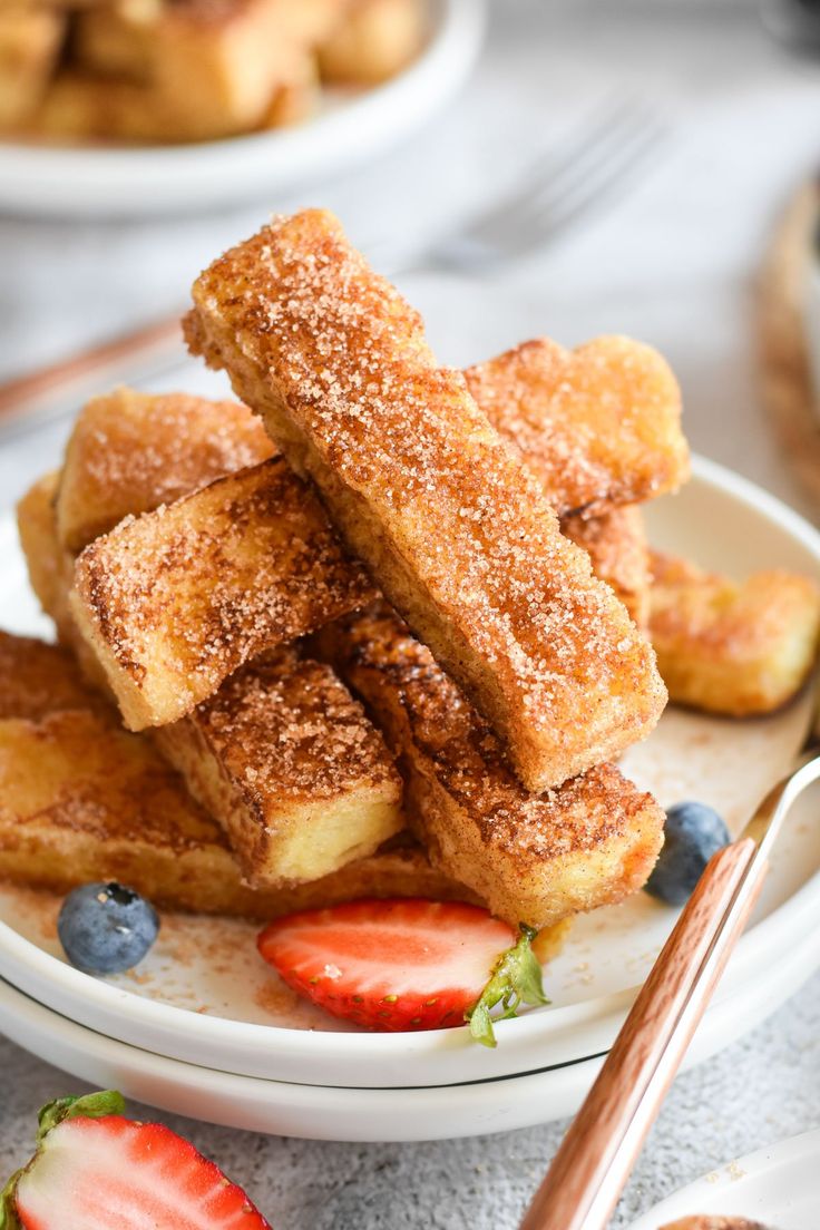 some sugared pastries are on a plate with strawberries and blueberries next to them