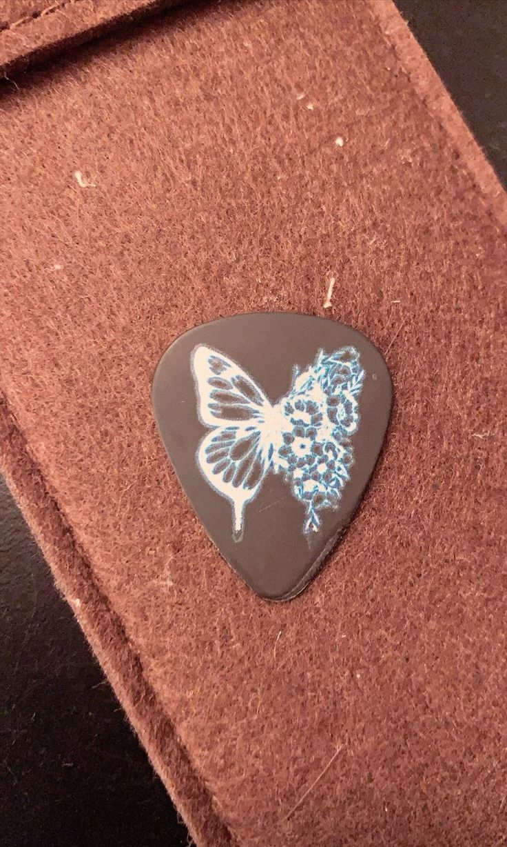 a guitar pick with a butterfly painted on it's side sitting on a piece of brown felt