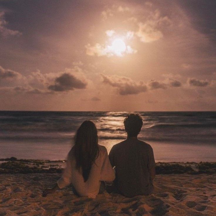 two people sitting on the beach watching the sun go down