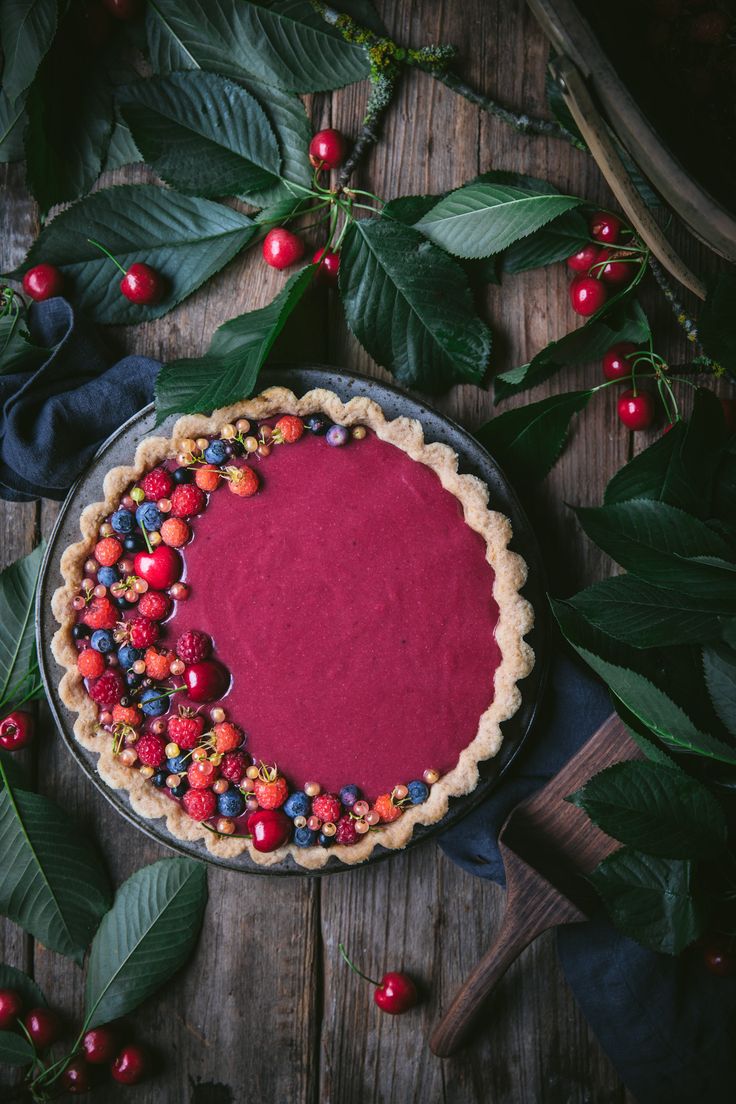 a pie with berries on it sitting next to leaves and red berry sauce in the middle