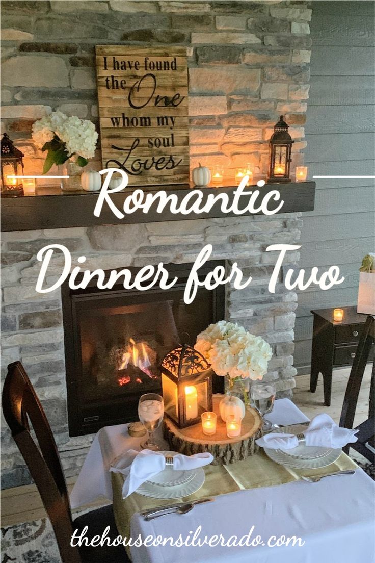 a dinner table with candles and flowers on it, in front of a stone fireplace