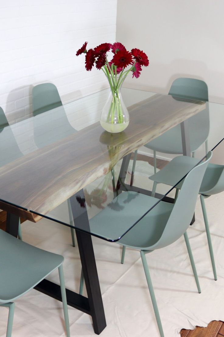 a glass table with blue chairs and a vase filled with flowers on top of it