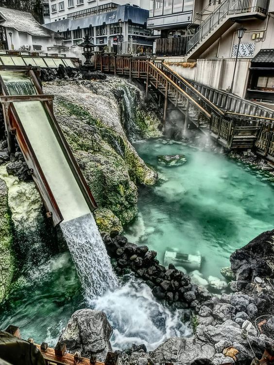 the water is green and flowing into the river, with buildings in the back ground