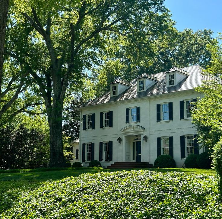 a large white house sitting on top of a lush green field next to trees and bushes