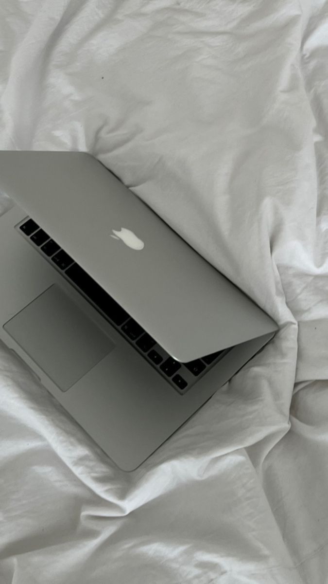 an open laptop computer sitting on top of a white bed cover covered in sheets and pillows