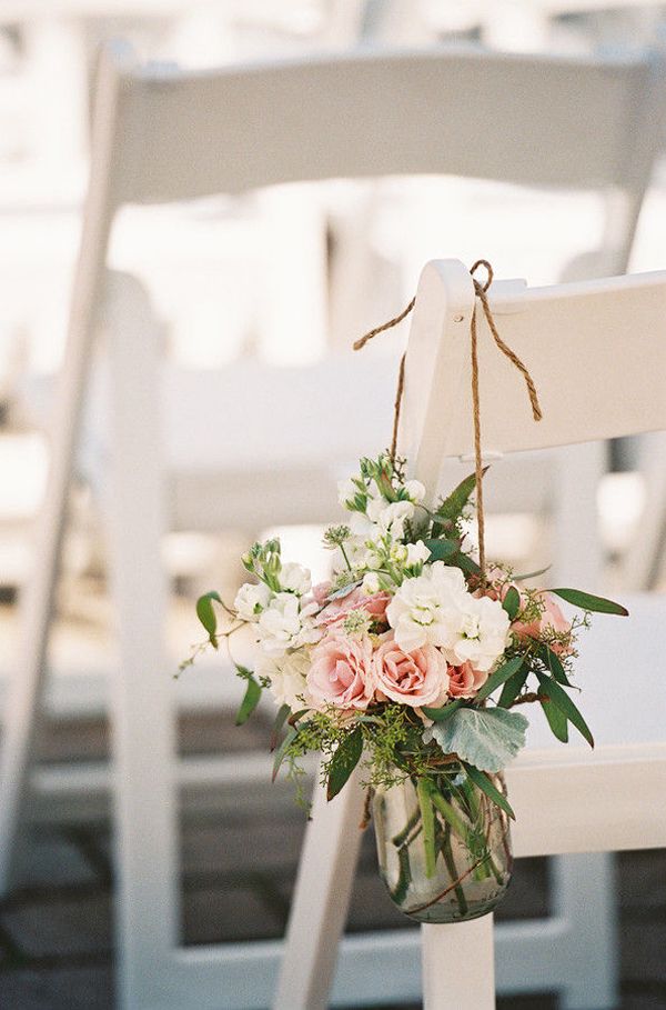 a bouquet of flowers is hanging from the back of a white chair at an outdoor ceremony