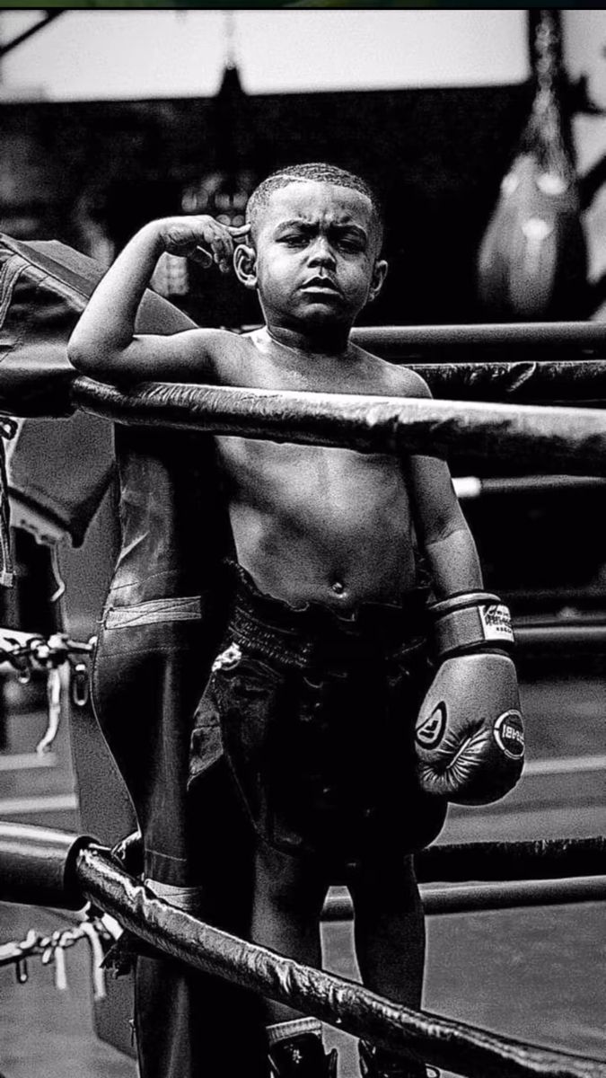 a black and white photo of a young boy with boxing gloves on his head standing in the ring