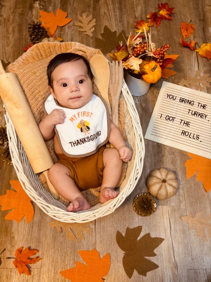 a baby is sitting in a basket with fall leaves