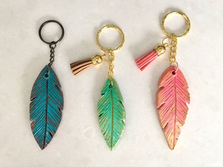 three different colored leaf shaped keychains on a white surface, one with a gold chain