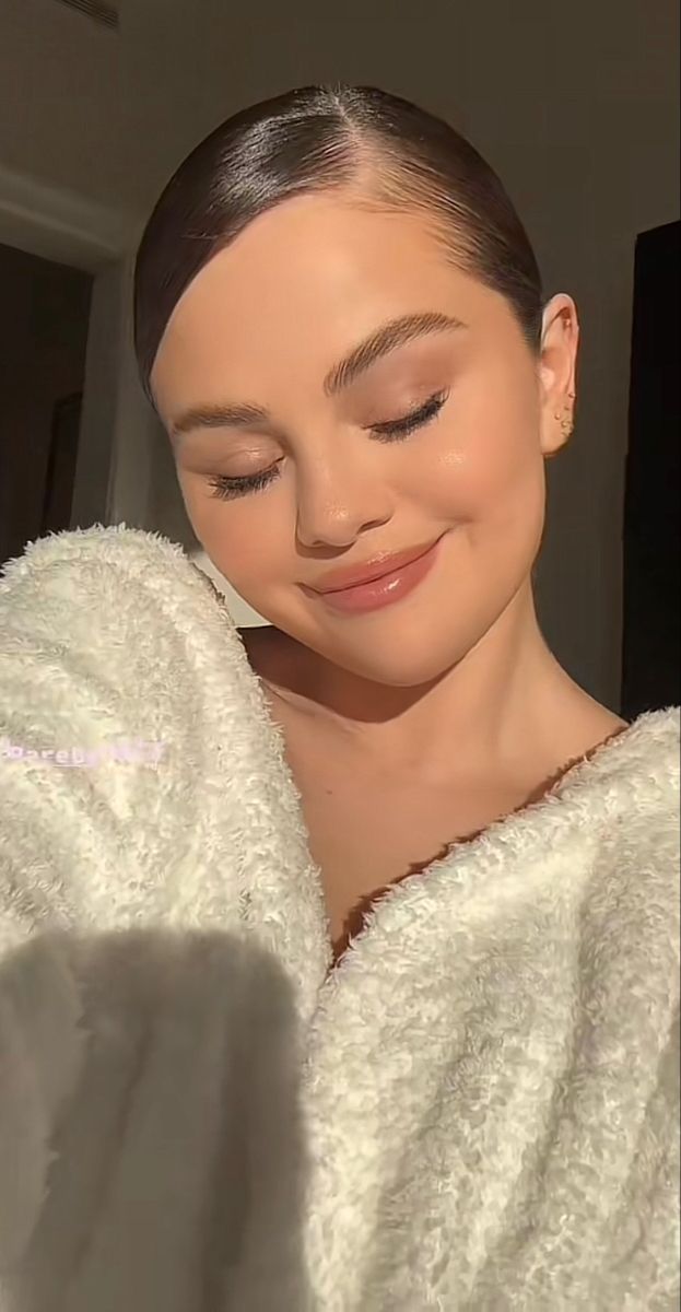 a woman in a bathrobe looking down at her cell phone while she is smiling