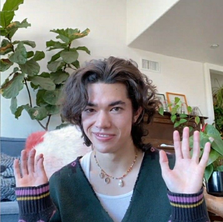 a young man is holding his hands up in the air while wearing a green sweater