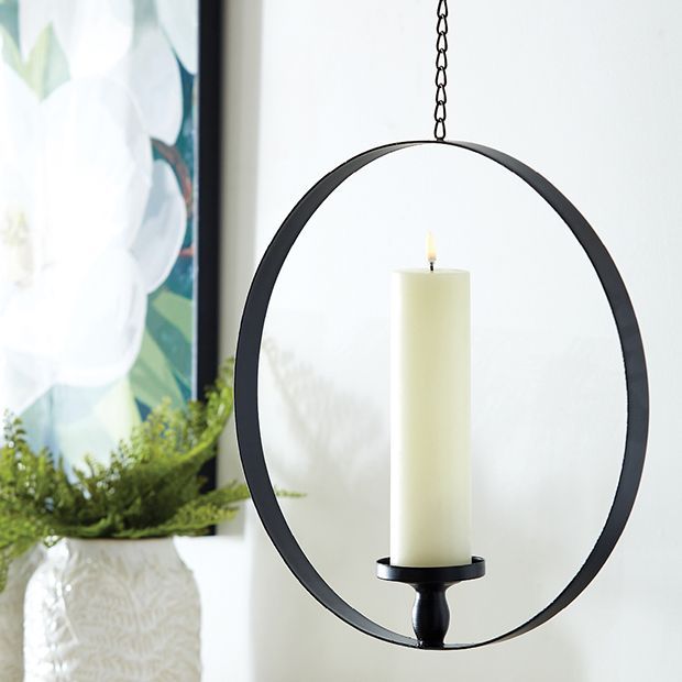 a candle is hanging from a circular metal holder on a shelf next to a potted plant