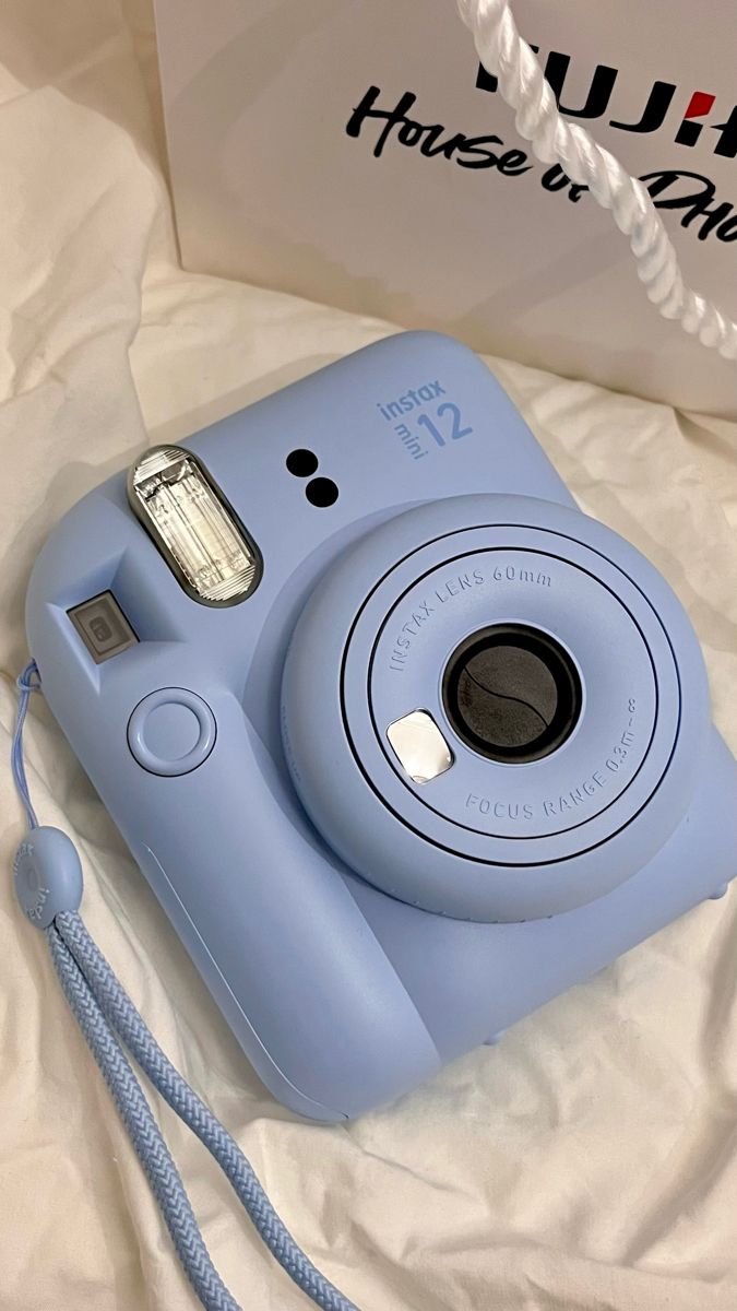 a blue digital camera sitting on top of a bed next to a bag and rope