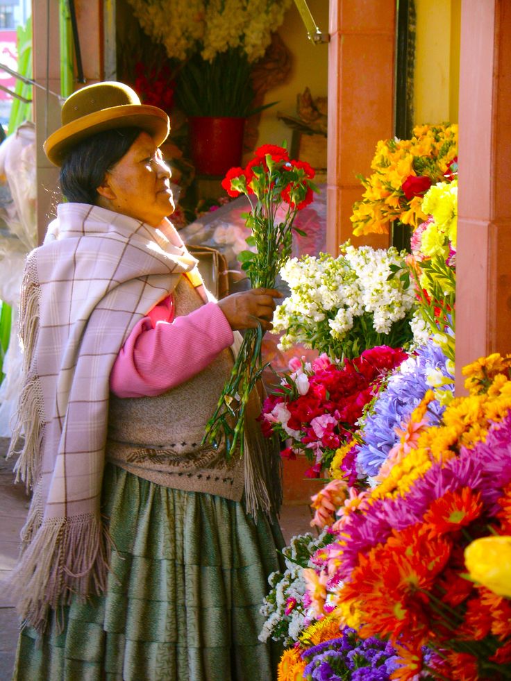 a woman holding flowers in her hands and looking at the flower display behind her is wearing a hat