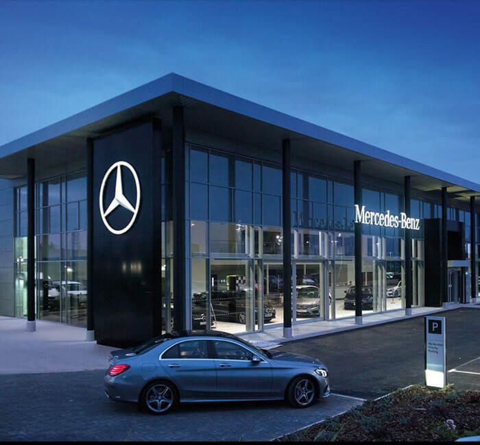 a car parked in front of a mercedes dealership at night with the lights on