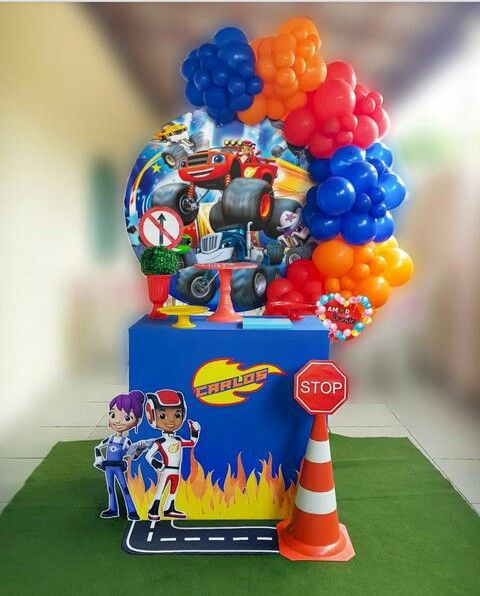 a birthday cake with balloons and cars on it's display stand in front of a traffic cone