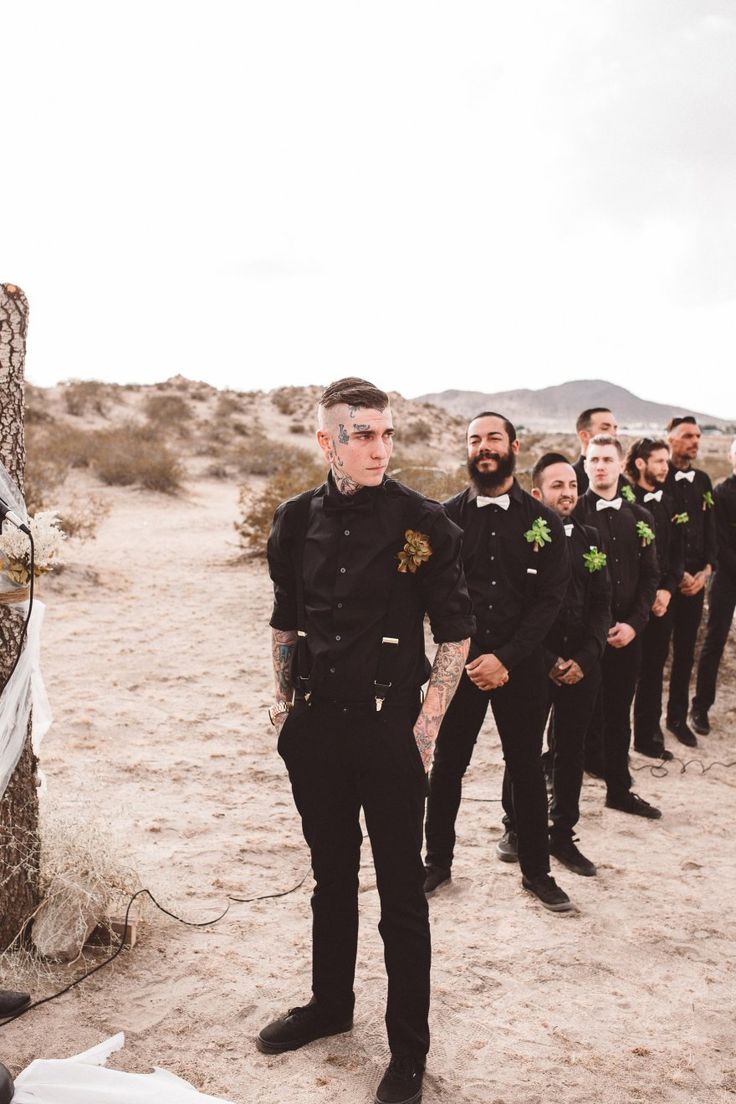 a group of men standing next to each other on top of a dirt field in front of a tree