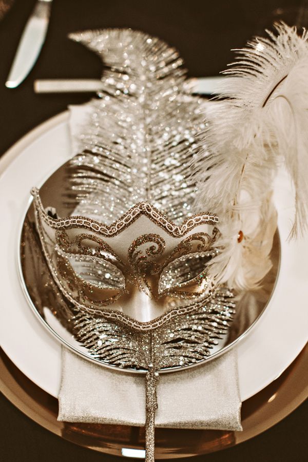 a masquerade mask sitting on top of a silver plate with feathers around it