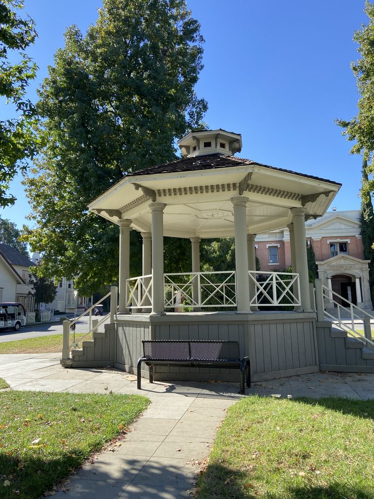 a white gazebo sitting on top of a sidewalk next to a lush green park